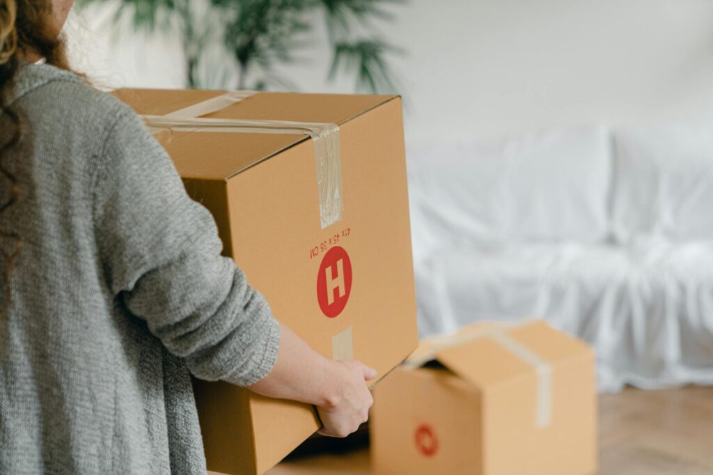 crop anonymous woman holding big box near sofa in apartment